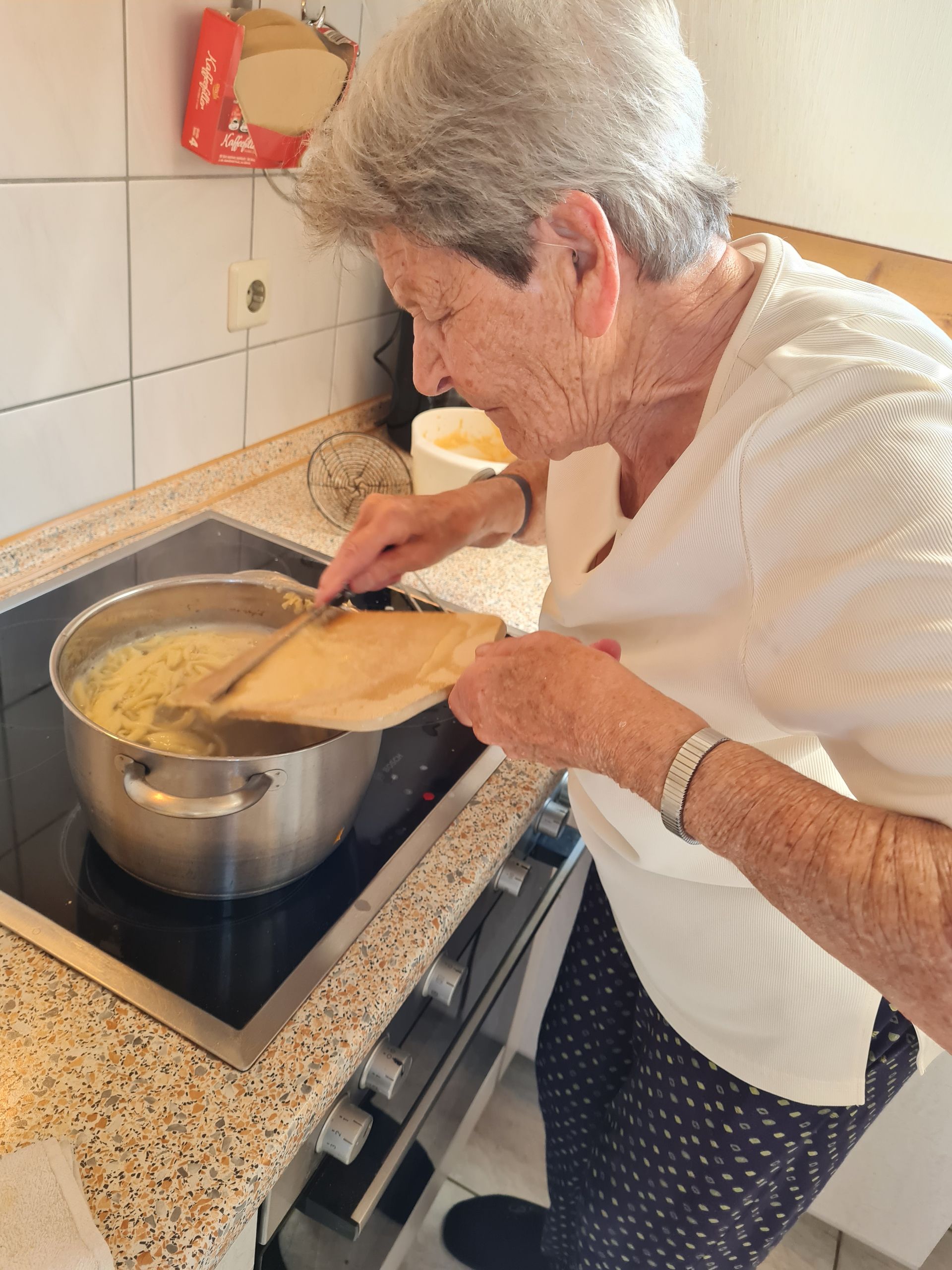 Eine ältere Person 95 Jahre, rührt in der Küche selbstgemachte Handspätzle in einem Topf auf dem Herd um.