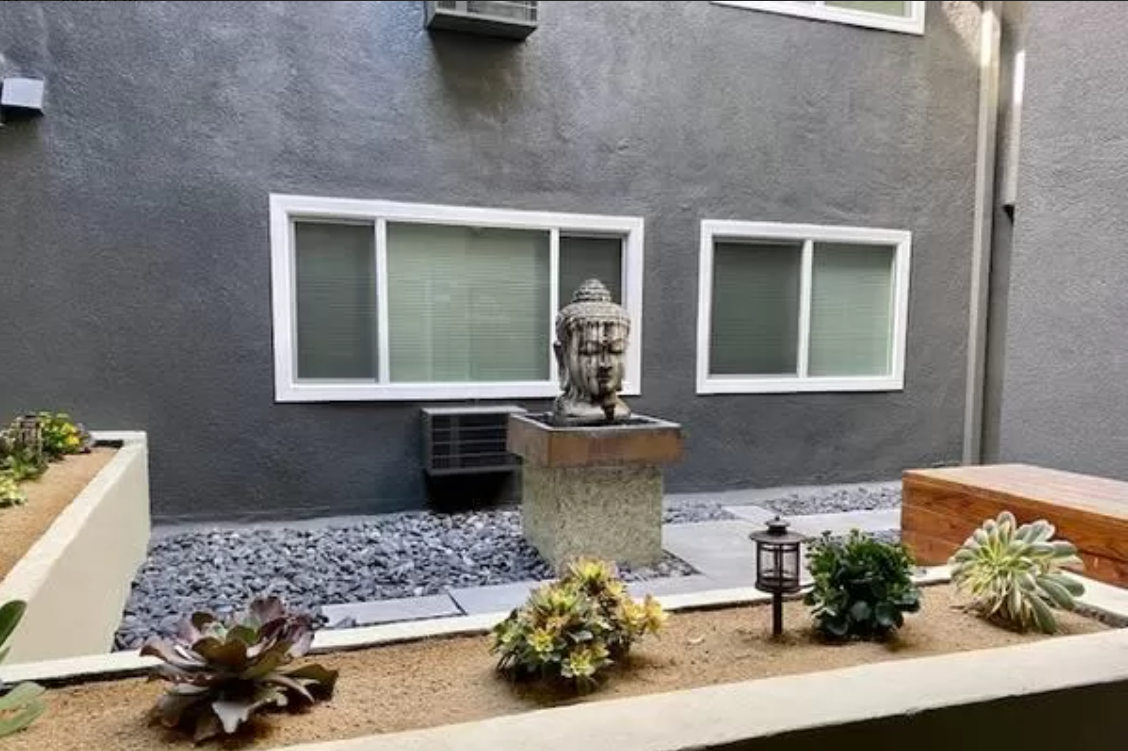 Courtyard with gray walls, windows, Buddha statue, and planters with succulents.