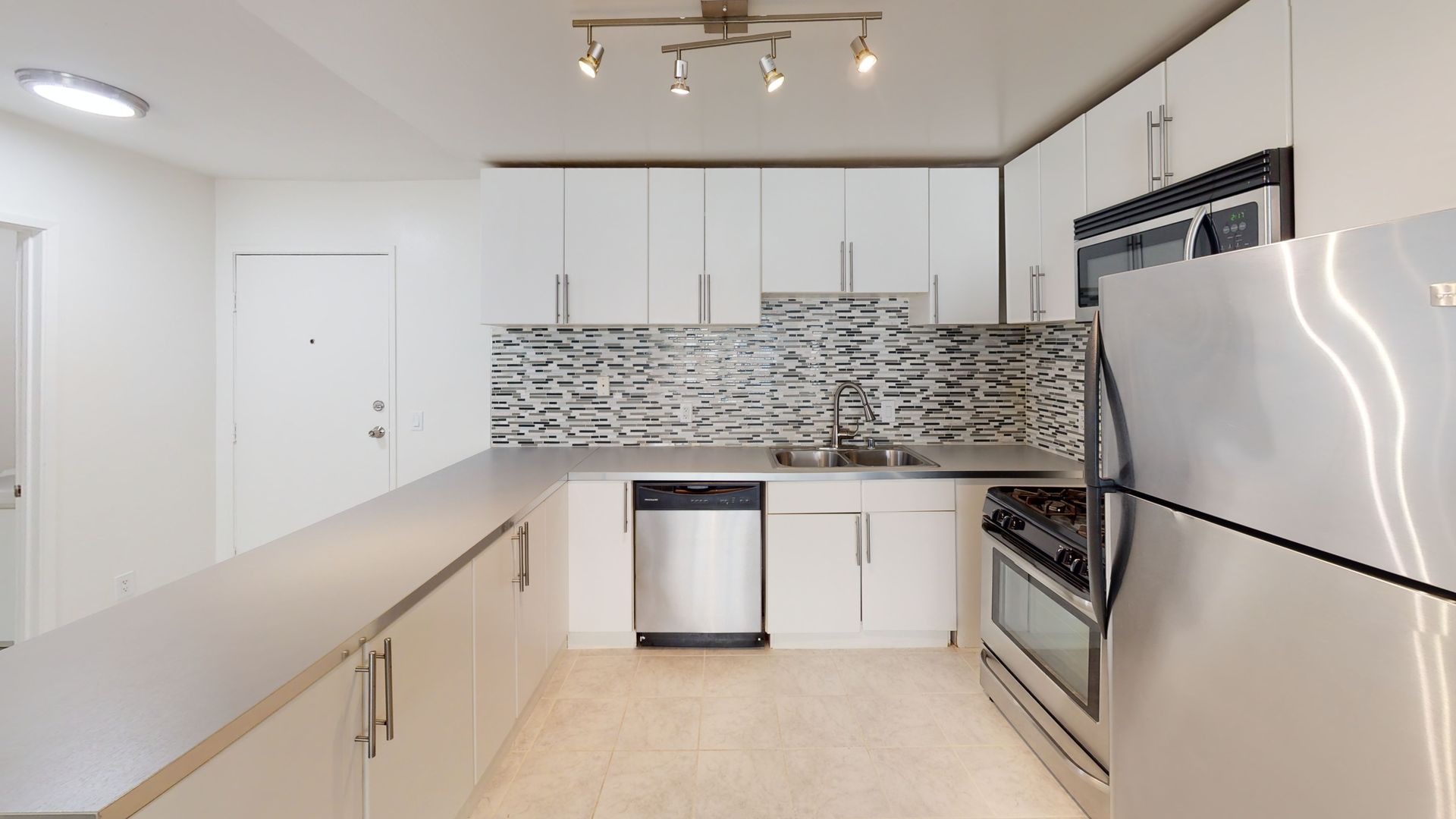 Modern kitchen with white cabinets, stainless steel appliances, and mosaic backsplash.