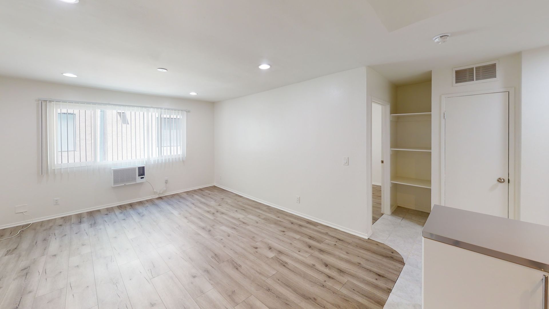 Empty, bright apartment interior with wooden floor, window, and built-in shelving.