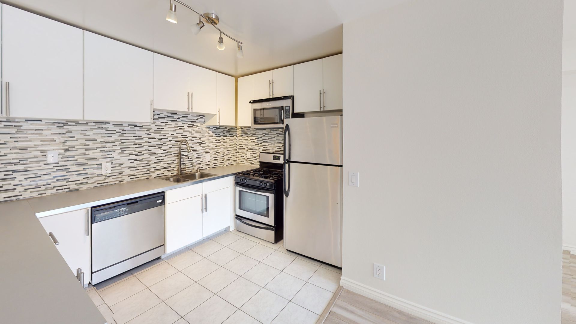 A white kitchen with stainless steel appliances, white cabinets, and a mosaic backsplash.