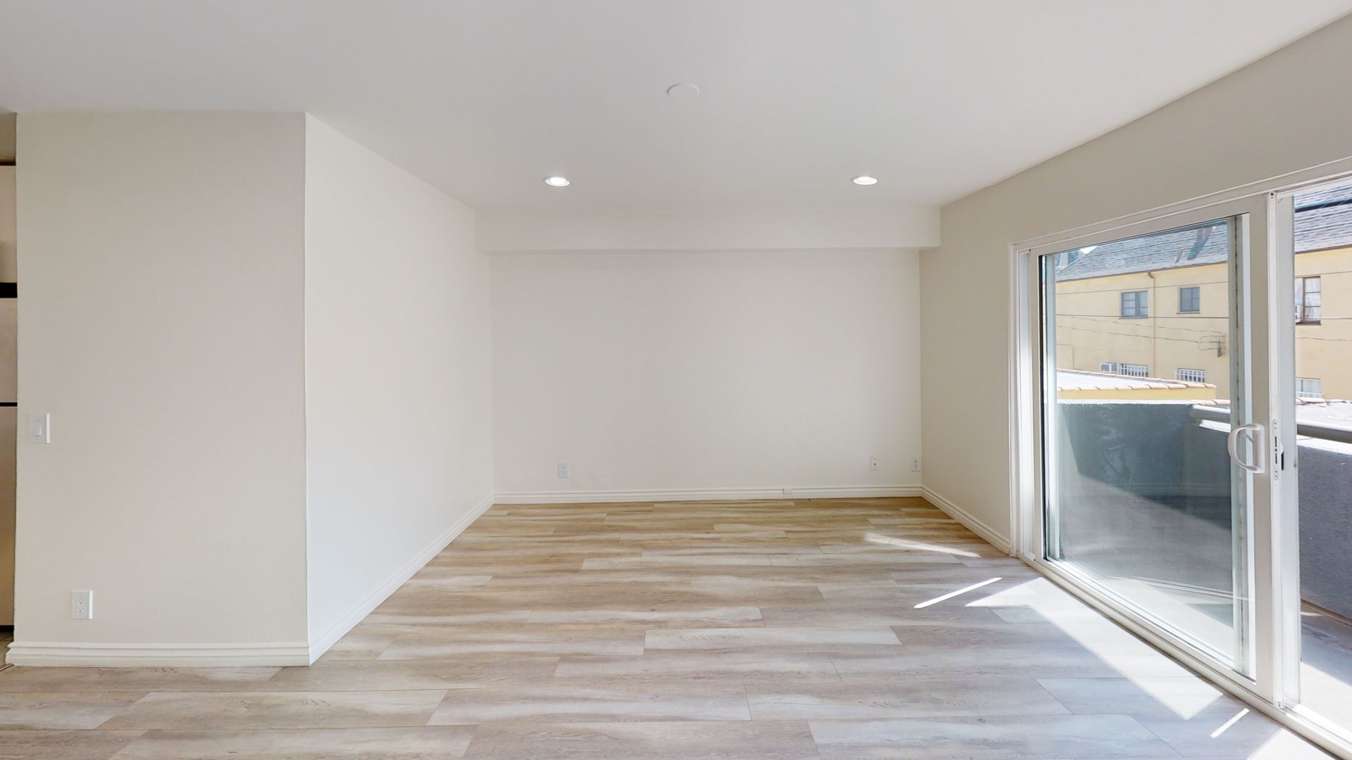 Empty room with wood-look flooring, white walls, and sliding glass door to a balcony.