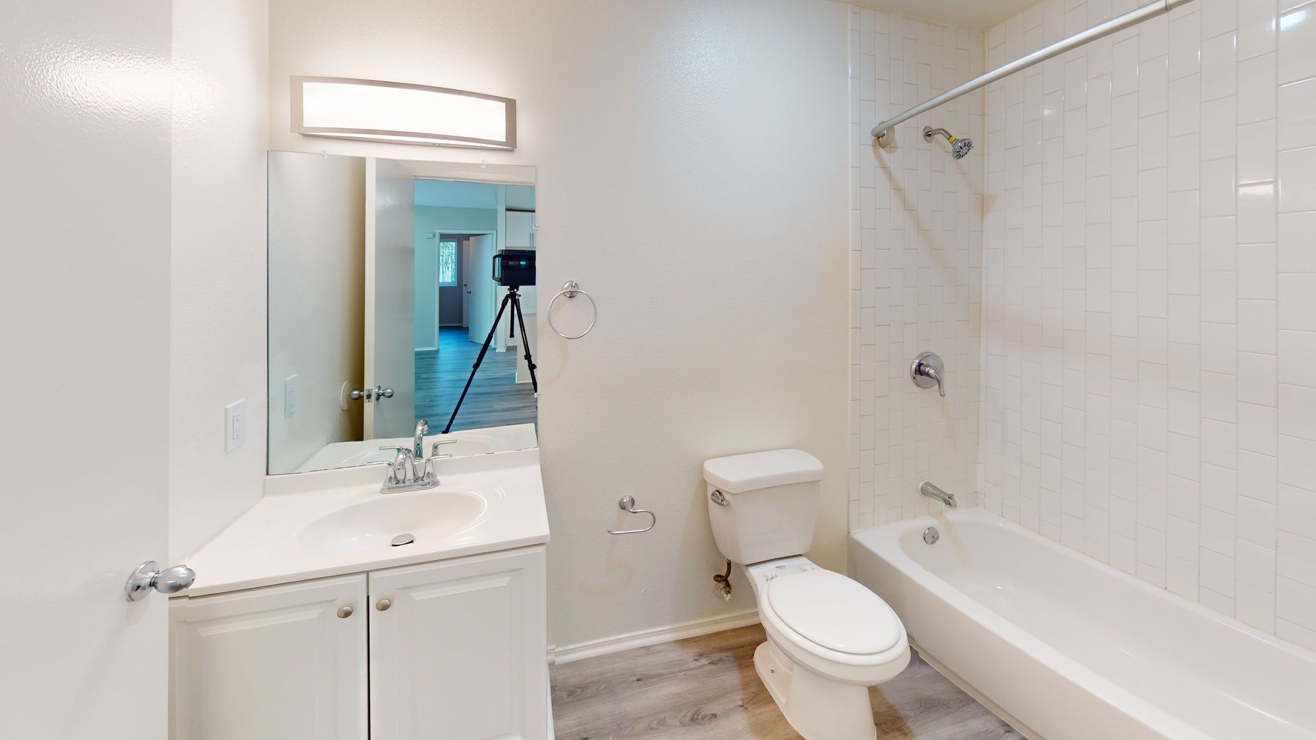 Bathroom with white walls, vanity, toilet, and bathtub. A mirror reflects a hallway.