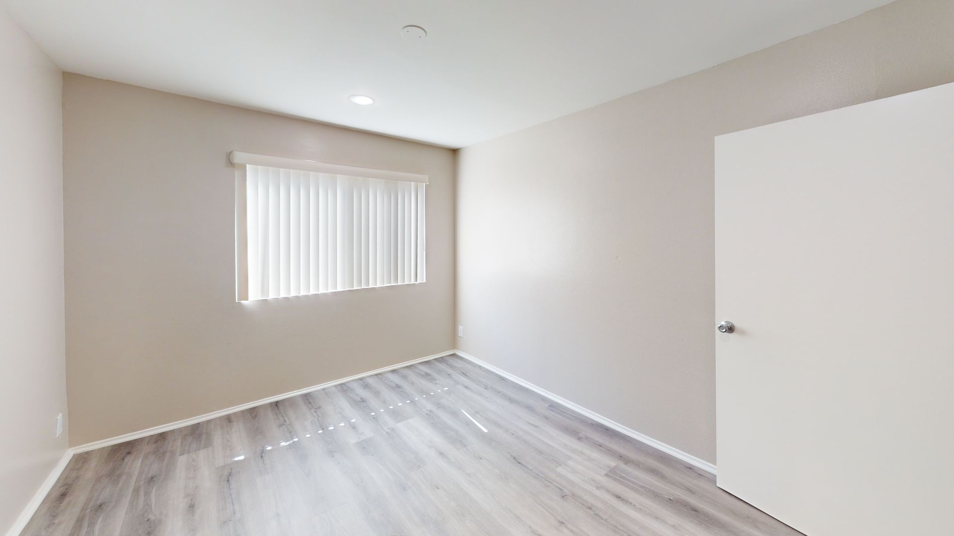 Empty room with gray wood-look flooring, a white door, and a window with blinds.