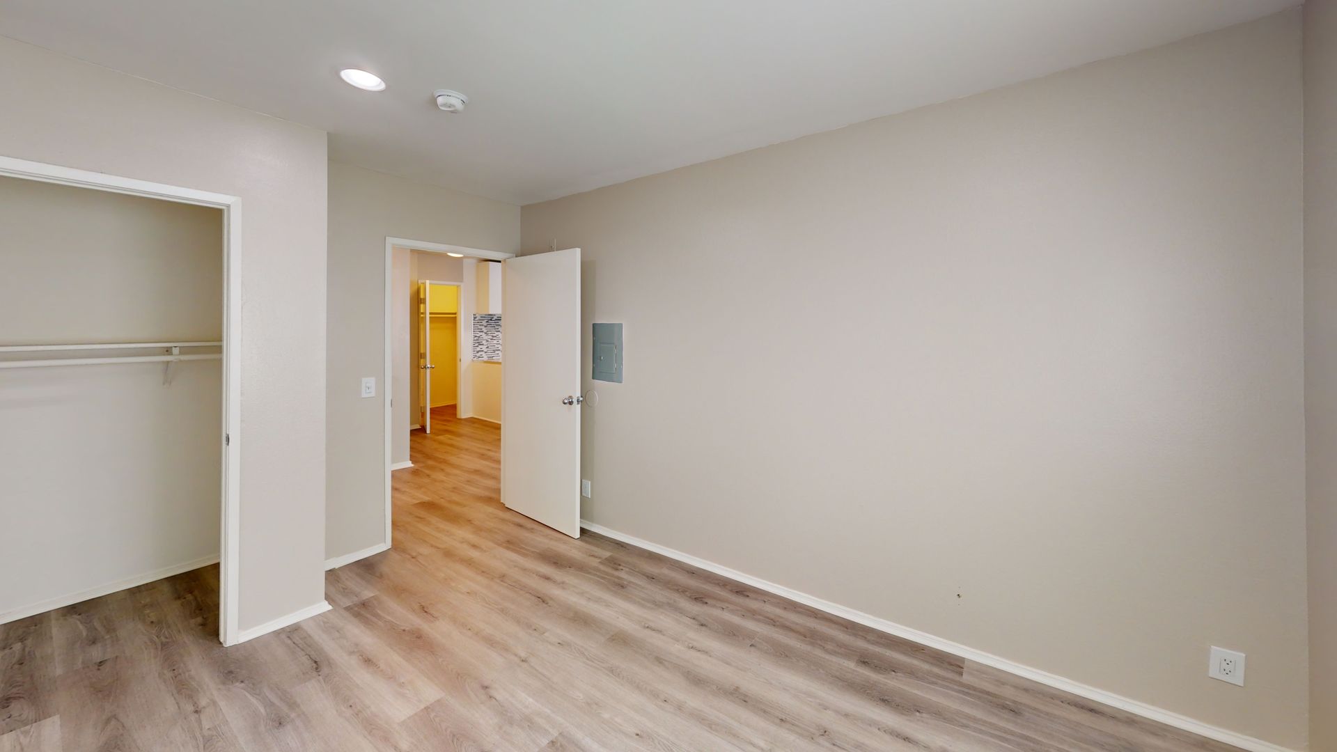 Empty bedroom with wood-look floors, closet, and a doorway leading to a hallway.