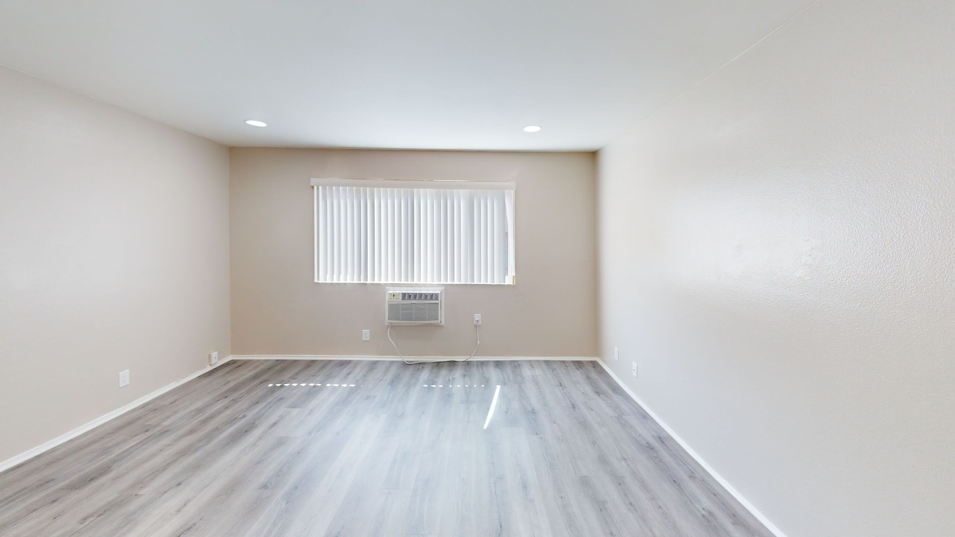 Empty room with gray wood-look floor, window with blinds, and an air conditioner.