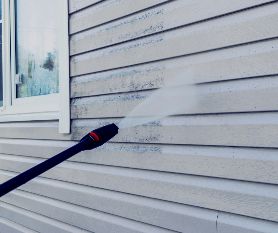 A person is cleaning the side of a house with a high pressure washer