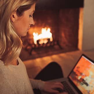 Woman using laptop in front of a fireplace.
