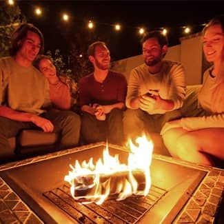 Group of people gathered around a fire pit, smiling and conversing outdoors at night.