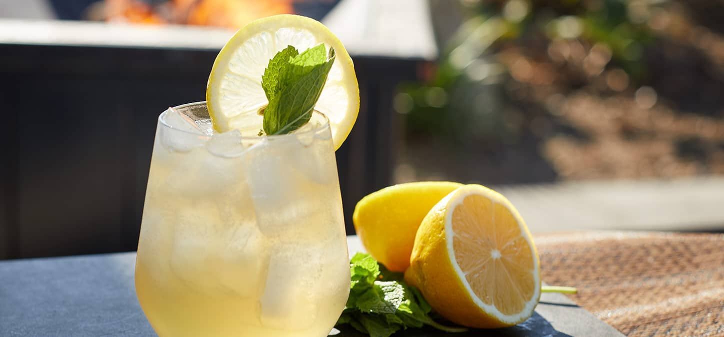 A glass of lemonade with ice and lemons on a table.