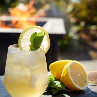 A glass of lemonade with ice and a slice of lemon on a table.