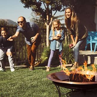 Family playing a game in a backyard with a fire pit burning.