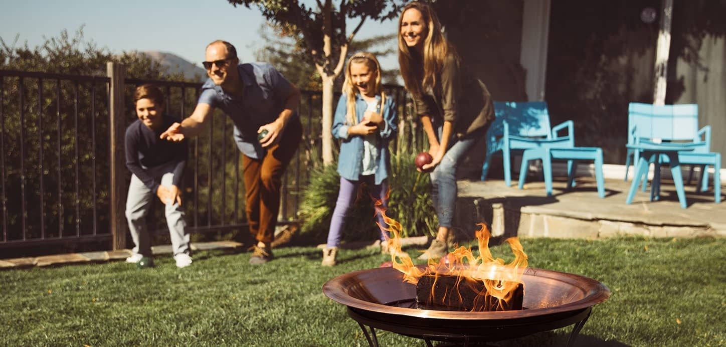 Family playing bocce lawn game near a fire pit in a backyard