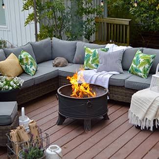 Outdoor sectional seating with cushions, fire pit, and decorative pillows on a wooden deck.