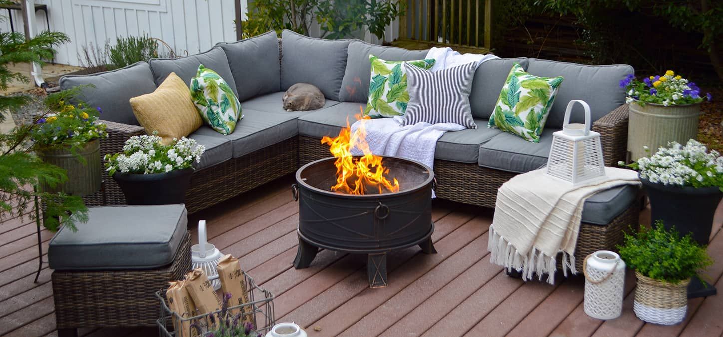 A sectional sofa around a round fire pit on a wooden backyard deck.