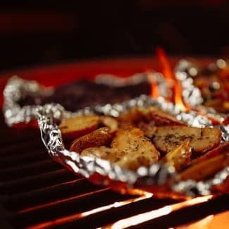 Aluminum foil packets with vegetables grilling over hot coals.