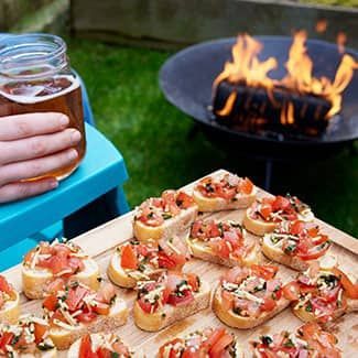a wooden board of bruscetta is in front of a fire pit
