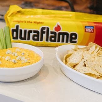 Buffalo chicken dip with tortilla chips in front of a packaged duraflame 6lb firelog