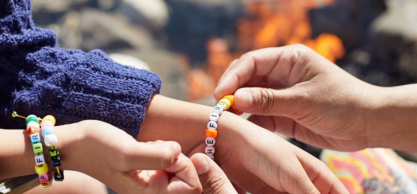 A person is putting a handmade bracelet on another person 's wrist.