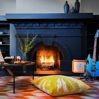 Black fireplace with burning fire, guitar, orange amp, and yellow floor cushion.