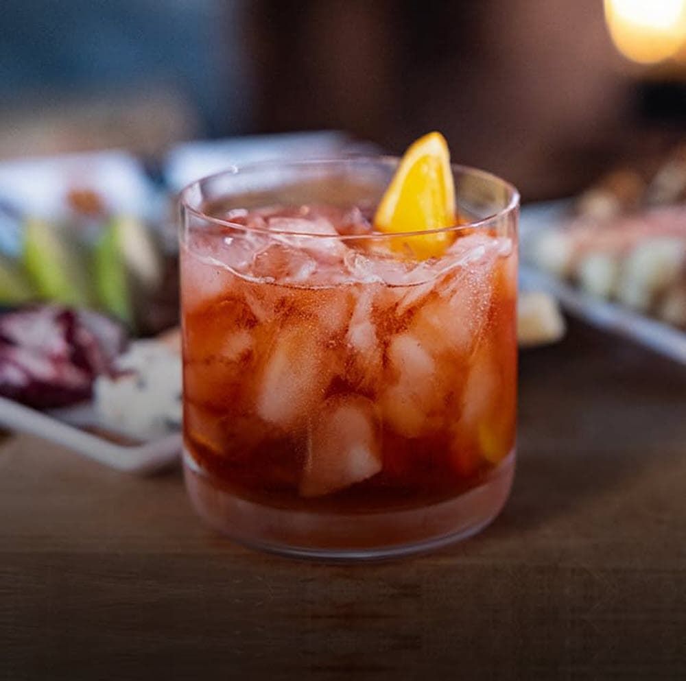 A close up of a winter negroni with ice and an orange slice on a table.