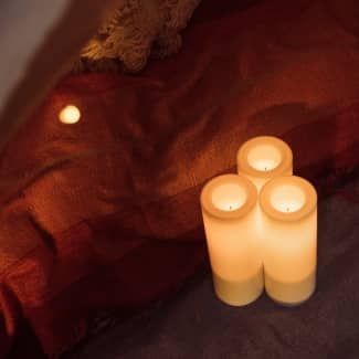 Three lit, flameless candles next to a blurred red background with a light.