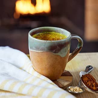 A cup of golden almond milk latte is sitting on a table in front of a fireplace.