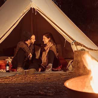 Couple in a tent, smiling, near a campfire at night.