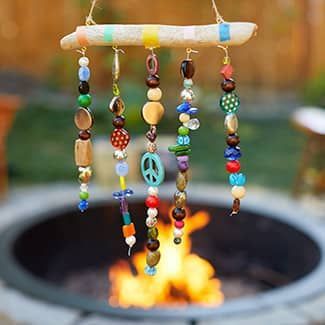 Beaded wind chime hanging above a fire pit, with colorful beads and a driftwood base.