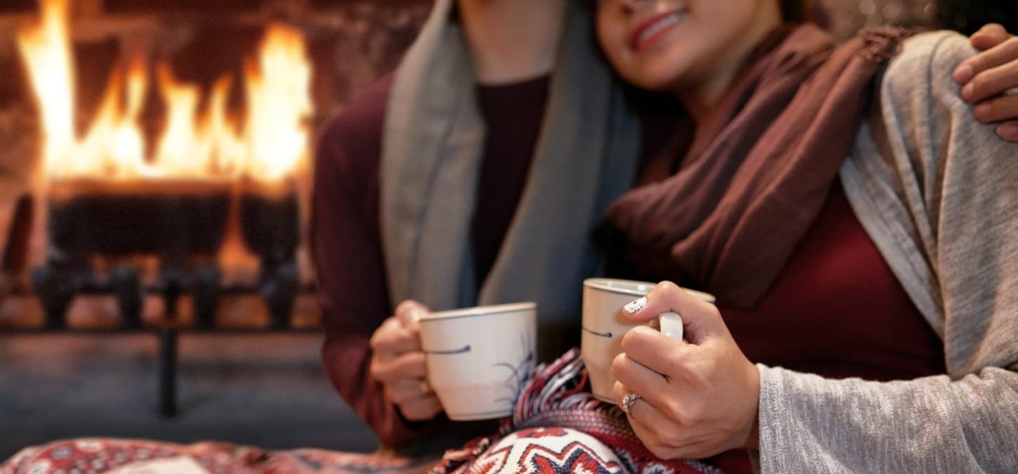 Two people are sitting in front of a fireplace holding cups of coffee.