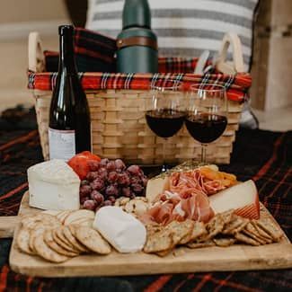 A wooden cutting board topped with cheese , crackers , grapes , and wine glasses.