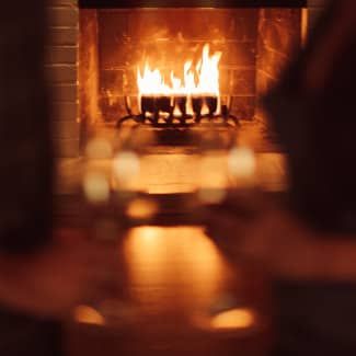 Fireplace with burning flames, two glasses are raised in front, blurred.