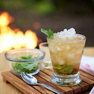 A mint julep garnished with mint leaves in front of a fire pit
