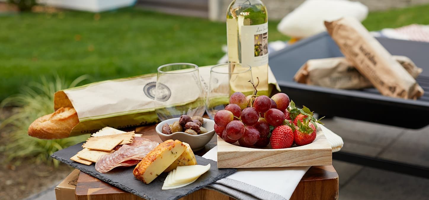 A table topped with a bottle of wine , grapes , cheese and crackers.