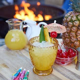 A pineapple cup filled with pina colada and umbrellas on a wooden table.