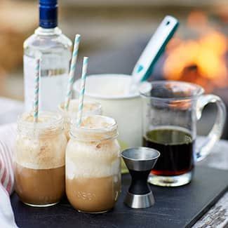 A tray of root beer floats with straws in front of a fire pit