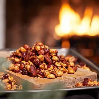 Candied and spiced nuts on a wooden board, with a blurred fireplace background.