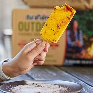 Hand holding spicy popsicle with a bite taken out, dipping into a plate of powder.