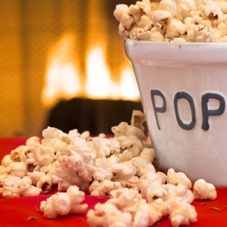A bowl of popcorn with the word pop written on it and a fireplace in the background