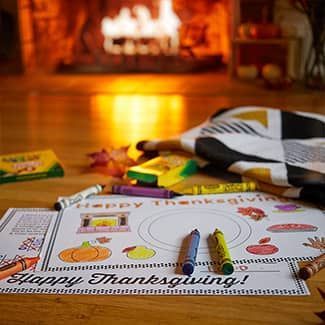 A happy thanksgiving coloring page with crayons and markers on a table in front of a fireplace.