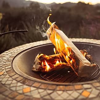 Fire pit with burning logs, outdoor setting, mosaic tile surround, flames visible.