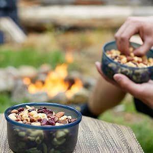 A person is holding a bowl of nuts in front of a fire.