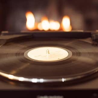 Vinyl record on a turntable with a fireplace in the background, lit with warm orange flames.