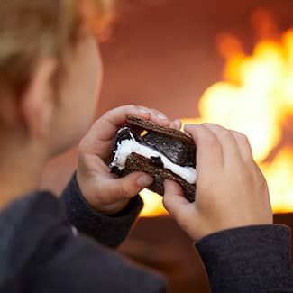 A child is holding a s'mores sandwich in front of a fire.