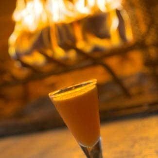 A wellness shot in a tall glass, lit by the glow of a warm fireplace.