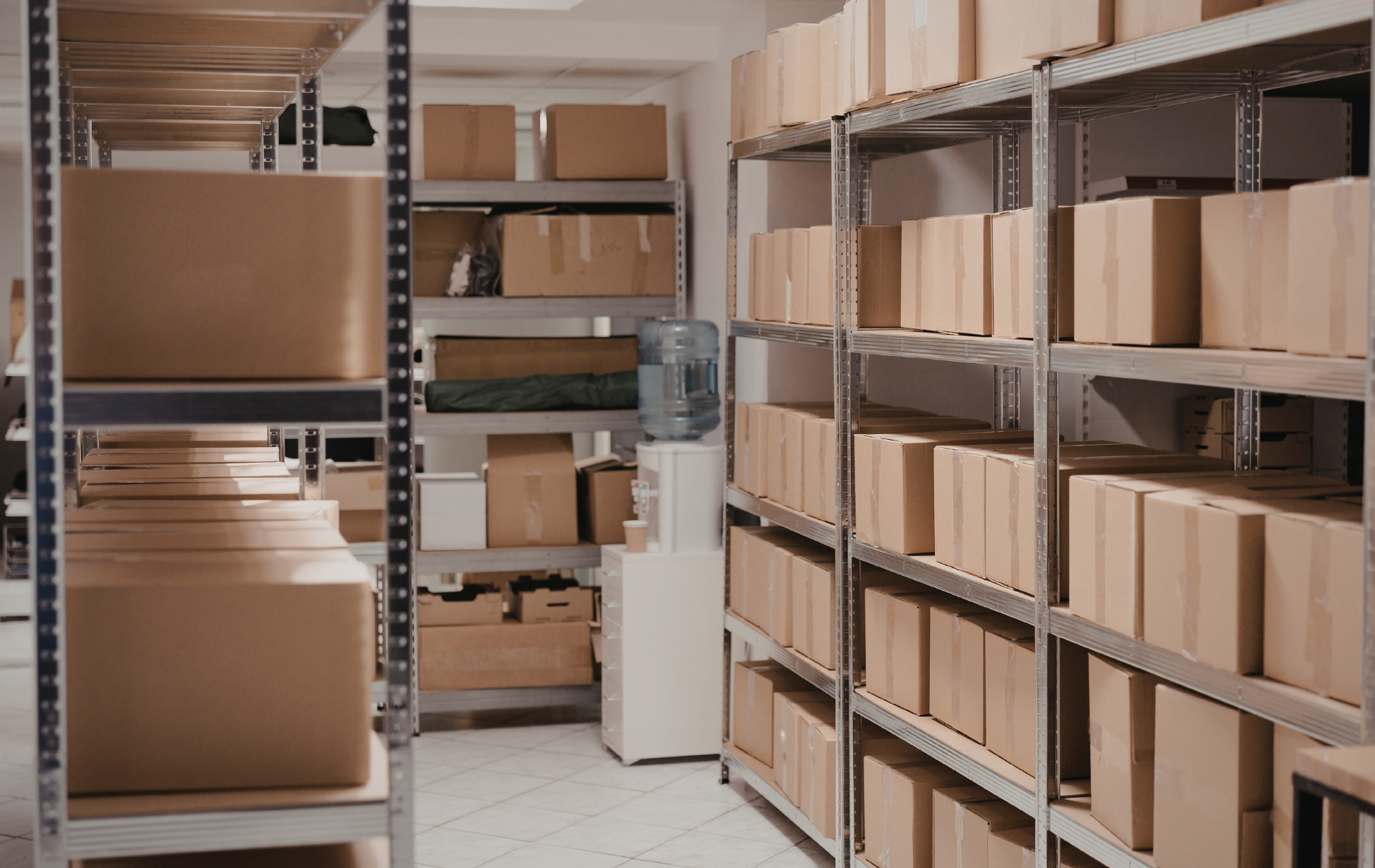 Rows of metal shelving units stocked with brown cardboard boxes in a warehouse-style storage room.