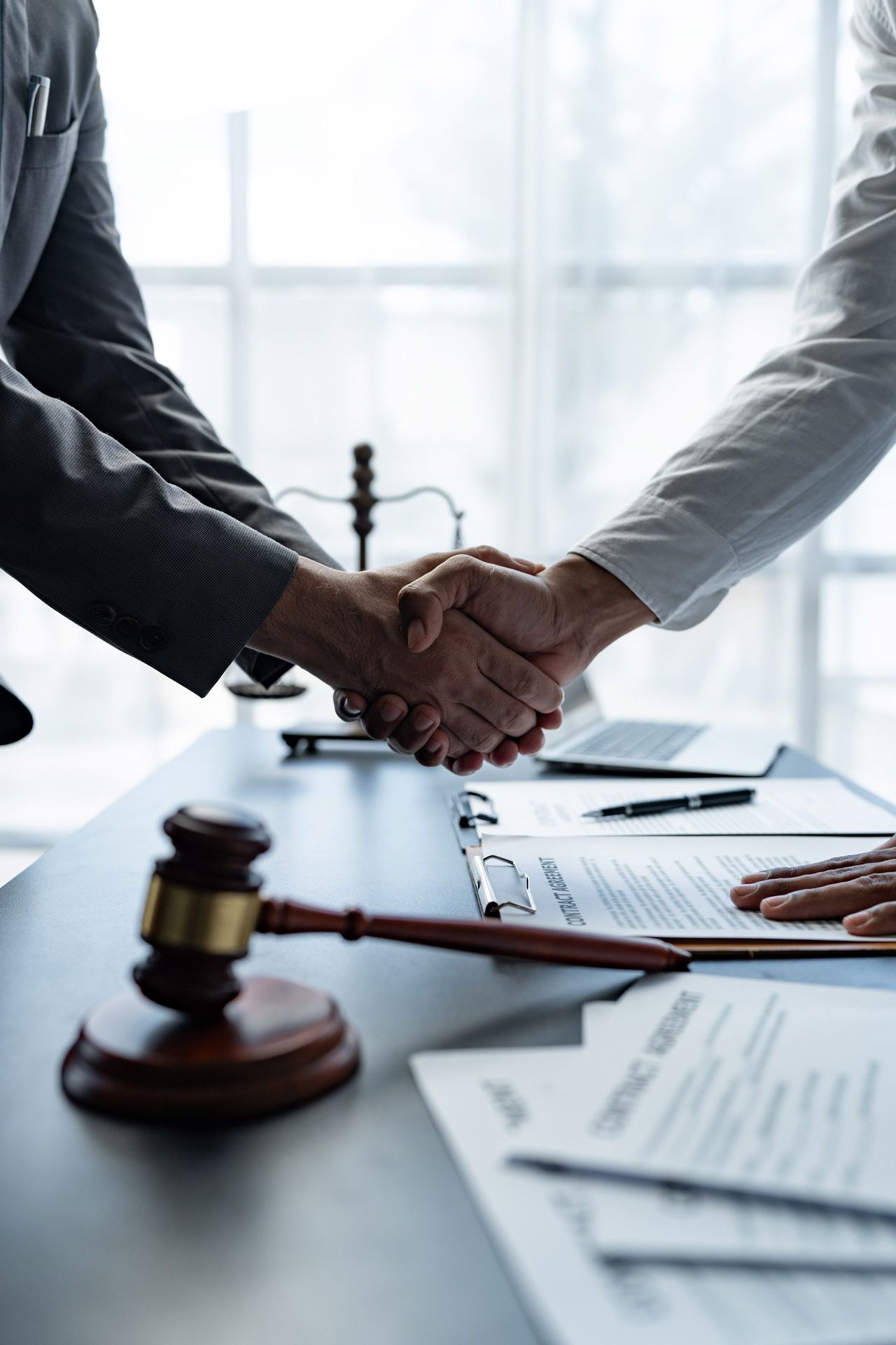 Two people shaking hands over a contract and gavel in an office setting.