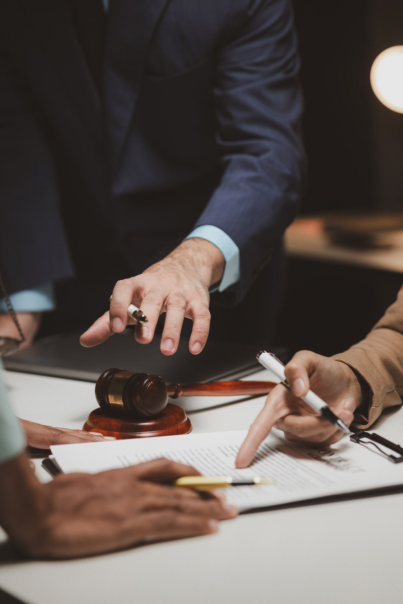 People in suits at a table pointing at documents, with a gavel in the center; legal setting.