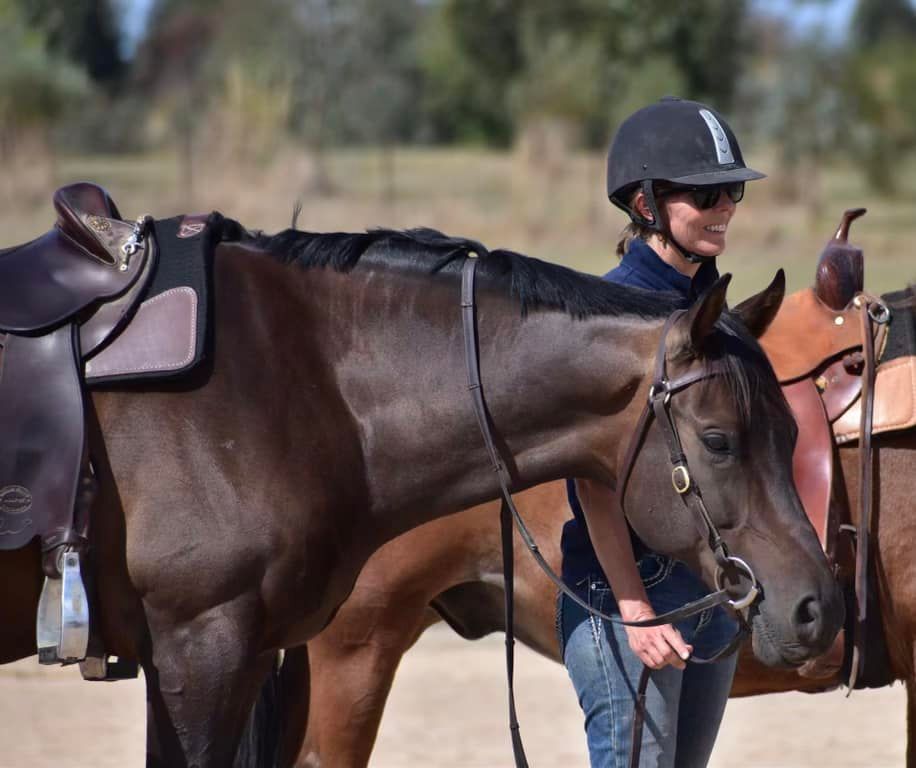 Woman in helmet with two saddled horses.