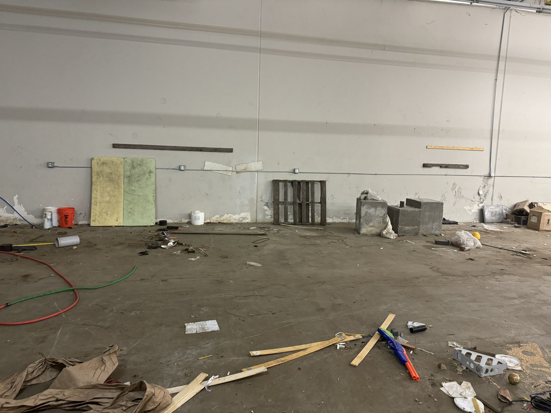 Empty, messy warehouse space with debris, pallet, and concrete blocks scattered on the floor.